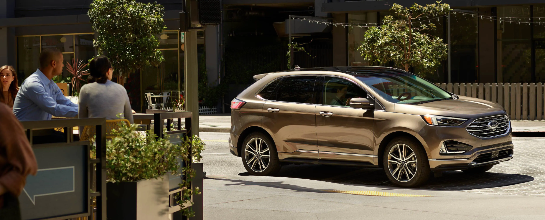 Image of a gold 2019 Ford Edge driving by a restaurant on a city street.